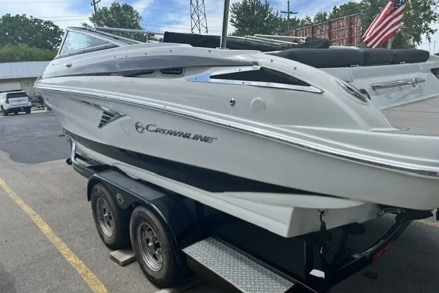 Slide: The Image of 2022 Crownline 240 SS boat on trailer, parked outdoors with American flag in background. - 2