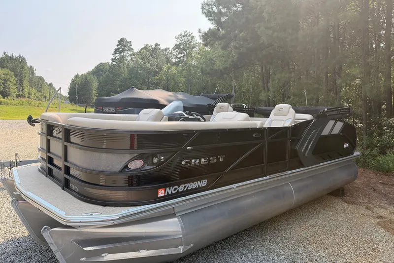 The Image of 2023 Crest Carribbean 250 SLC pontoon boat parked on gravel, surrounded by trees. - 0
