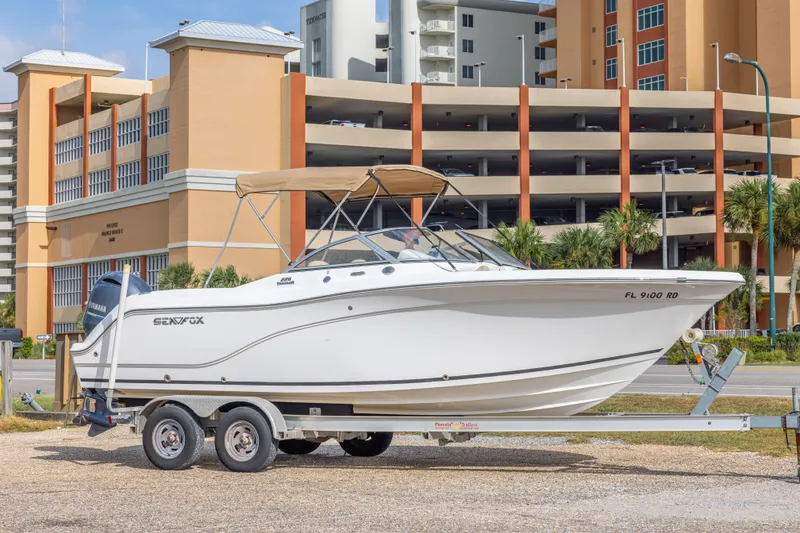 The Image of 2016 Sea Fox 226 Traveler boat on trailer, parked near a multi-story building. - 0