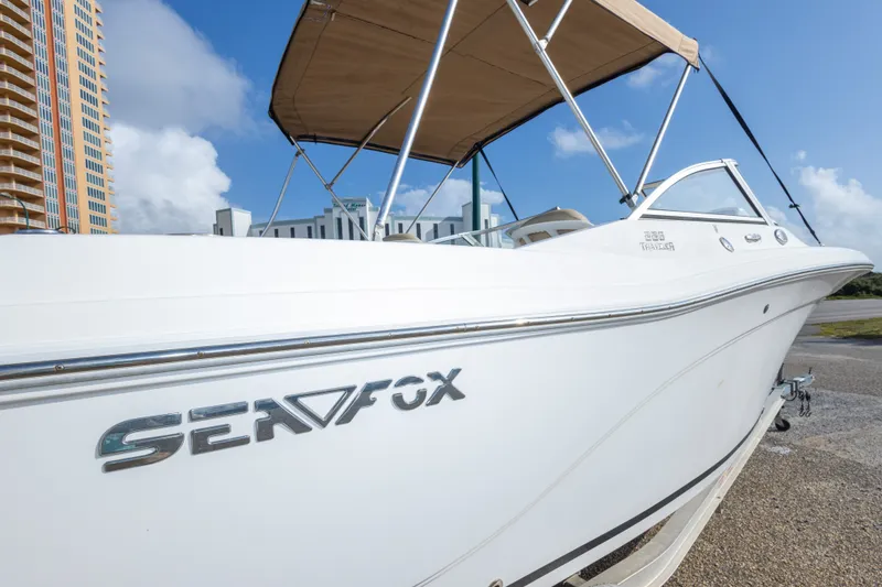 Slide: The Image of 2016 Sea Fox 226 Traveler boat with canopy, parked near buildings under a clear blue sky. - 46