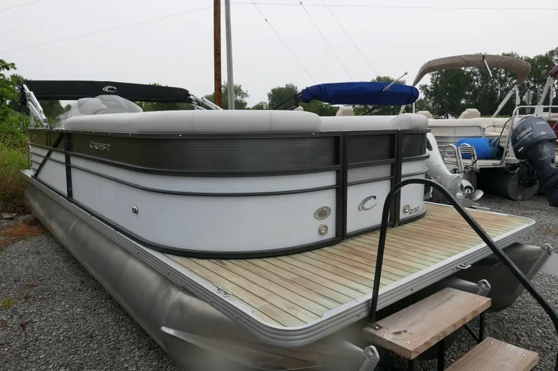 Slide: The Image of 2018 Crest II pontoon boat with wooden deck, parked on gravel. - 1
