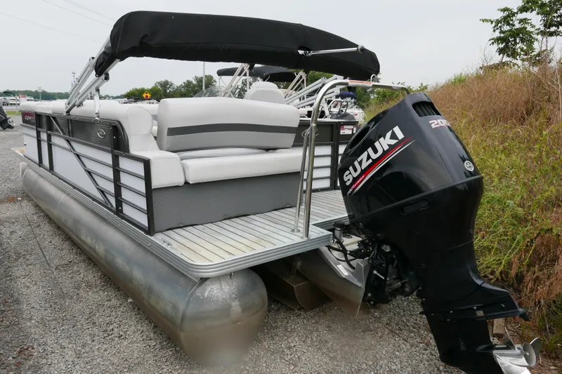 Slide: The Image of 2018 Crest II pontoon boat with Suzuki outboard motor, parked on gravel. - 2