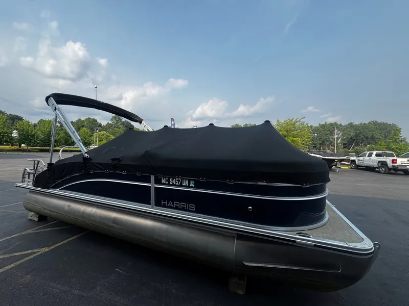 Slide: The Image of A 2021 Harris Cruiser 230 pontoon boat with a black cover, parked in a lot. - 26