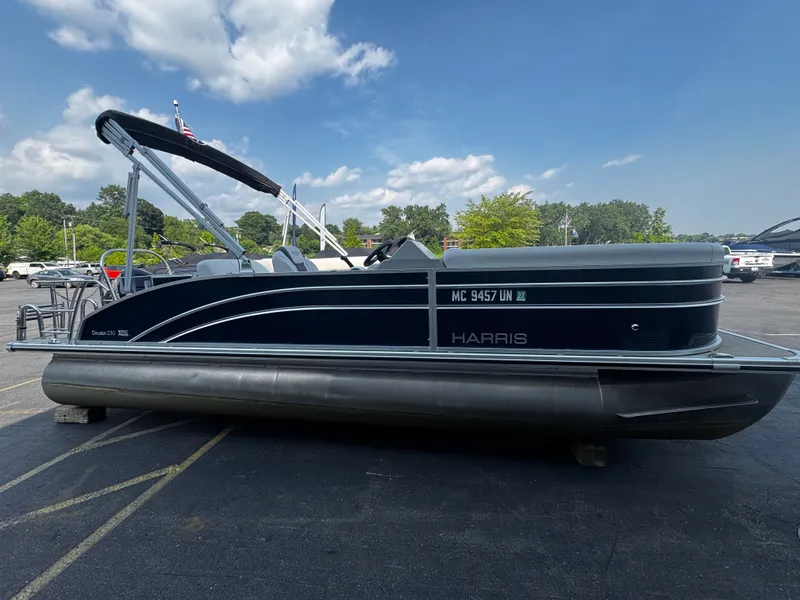 The Image of A 2021 Harris Cruiser 230 pontoon boat is parked in a lot. It features a black canopy. - 0