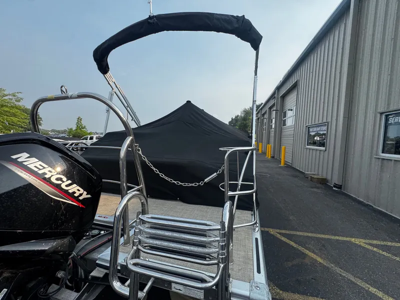 Slide: The Image of A 2021 Harris Cruiser 230 with a black cover and Mercury engine, parked beside a building. - 28