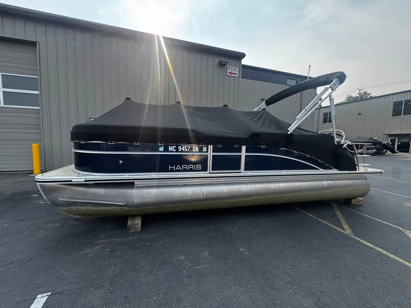 Slide: The Image of A 2021 Harris Cruiser 230 pontoon boat with a black cover, parked in front of a building. - 30