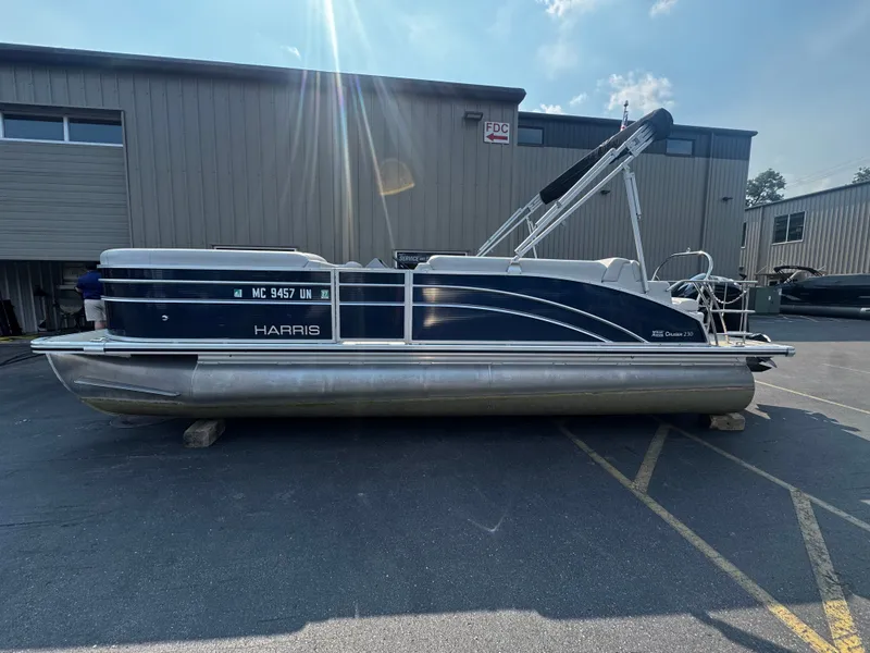 Slide: The Image of A 2021 Harris Cruiser 230 pontoon boat is parked on a lot. It features a blue and white design. - 5