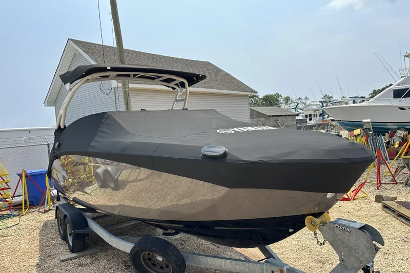 Slide: The Image of 2023 Yamaha Boats 252SE covered on trailer, parked outdoors near other boats. - 16