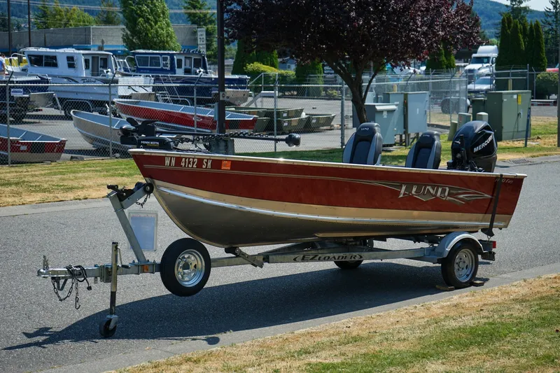Slide: The Image of 2015 Lund 1400 Fury SS boat on trailer, parked near marina with other boats. - 15