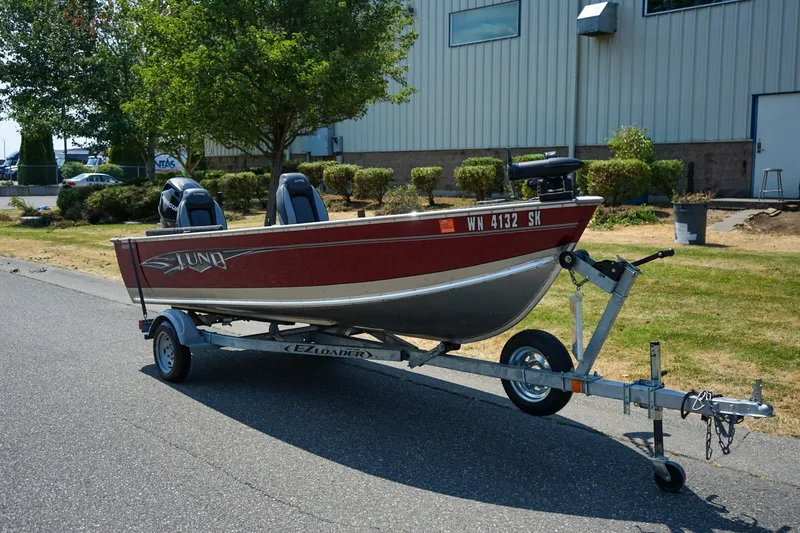 The Image of 2015 Lund 1400 Fury SS boat on trailer, parked outdoors near industrial building. - 1