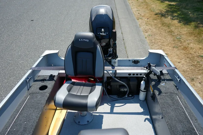 Slide: The Image of 2015 Lund 1400 Fury SS boat interior with seating and motor, parked on roadside. - 8