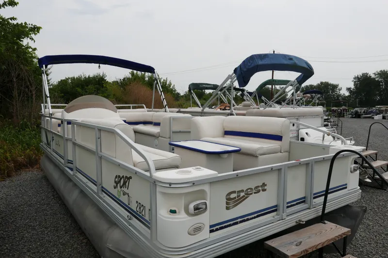 The Image of 2002 Crest 20 Sport pontoon boat with white seating and blue accents, parked outdoors. - 0