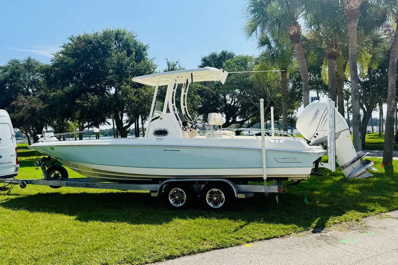 Slide: The Image of 2018 Boston Whaler 240 Dauntless boat on trailer, parked on grass with trees in background. - 3