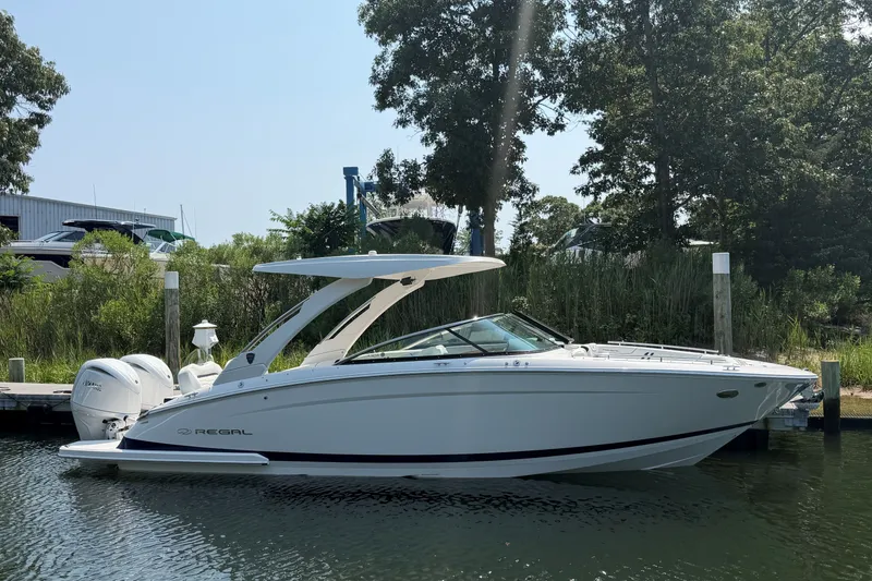 Slide: The Image of 2027 Regal LX9 boat docked by lush greenery and calm waters. - 1