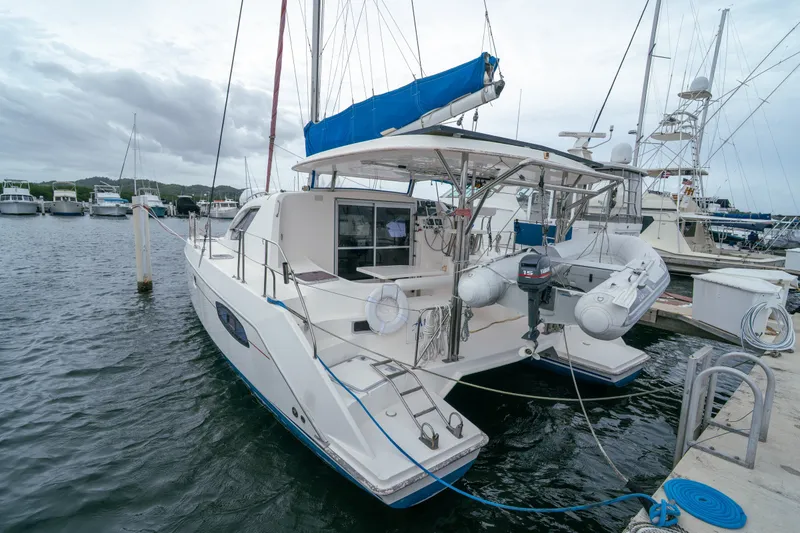 Slide: The Image of 2011 Leopard 38 catamaran docked at marina, featuring blue sail cover and inflatable dinghy. - 11