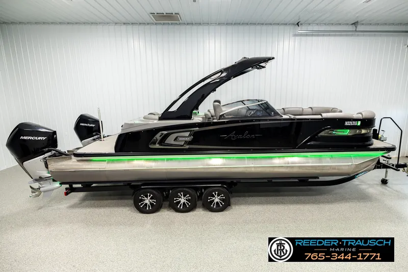 The Image of 2021 Avalon EXCALIBUR boat with dual Mercury engines, displayed indoors on a trailer. - 1