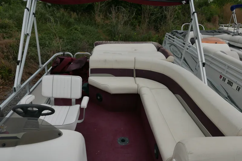 Slide: The Image of 2002 Avalon Tahoe Vista pontoon boat with white and maroon seating, docked near greenery. - 8