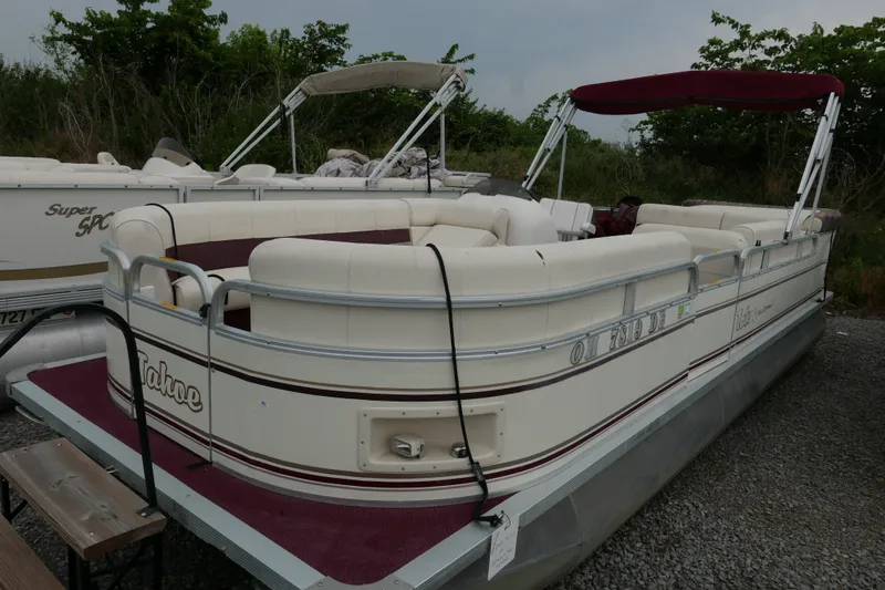 Slide: The Image of 2002 Avalon Tahoe Vista pontoon boat with maroon accents, parked on gravel. - 1