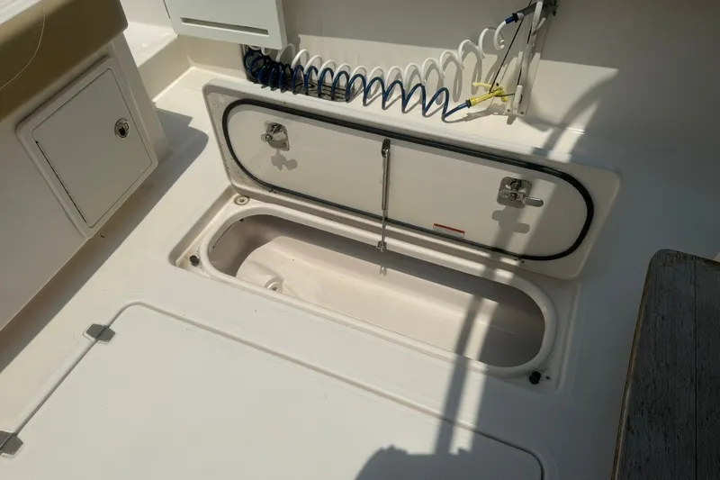 Slide: The Image of 2017 Pursuit S 408 Sport boat storage compartment with open hatch and coiled hose. - 24