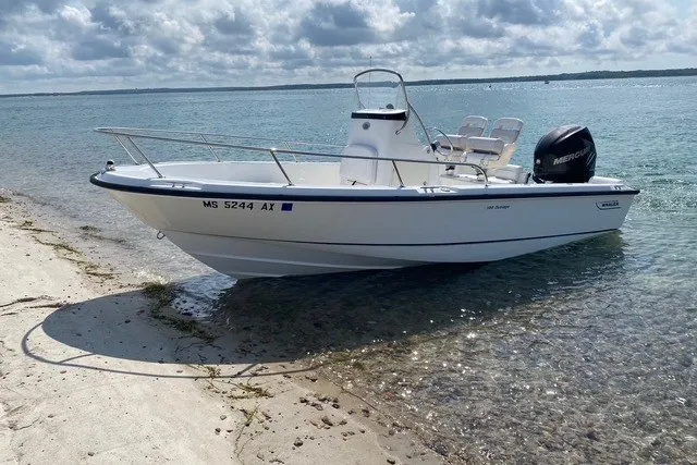 Slide: The Image of 2010 Boston Whaler 190 Outrage boat on sandy shore, clear water, and cloudy sky. - 1