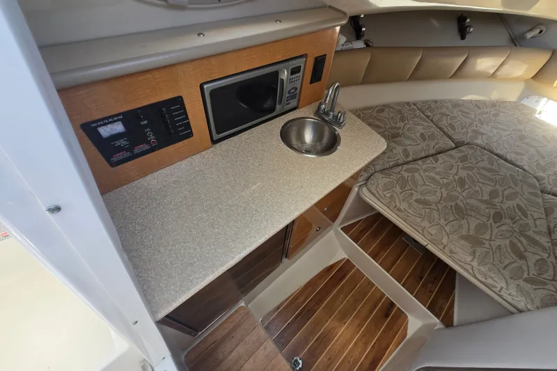 Slide: The Image of 2006 Robalo R265 Walkaround cabin interior with kitchenette, sink, and cushioned seating area. - 19