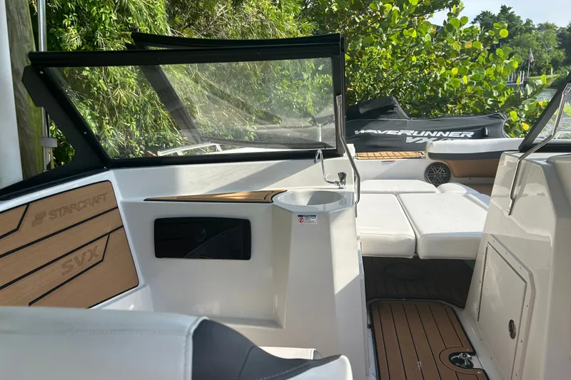 Slide: The Image of 2023 Starcraft SVX 191 OB boat interior with seating and sink, surrounded by lush greenery. - 19