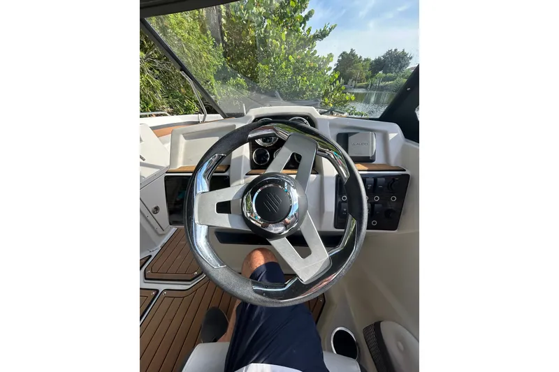 Slide: The Image of 2023 Starcraft SVX 191 OB boat steering wheel and dashboard, surrounded by lush greenery. - 13