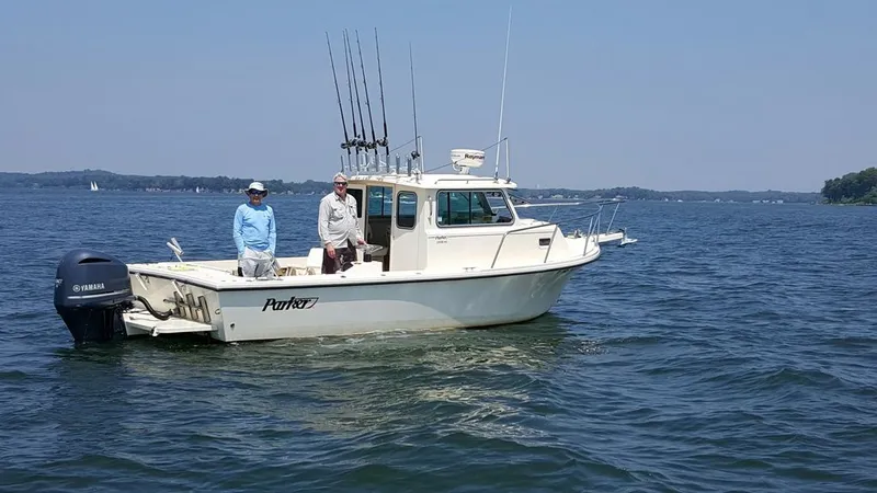 Slide: The Image of Two people stand on a Parker 2520 XL Sport Cabin boat on calm water. - 2