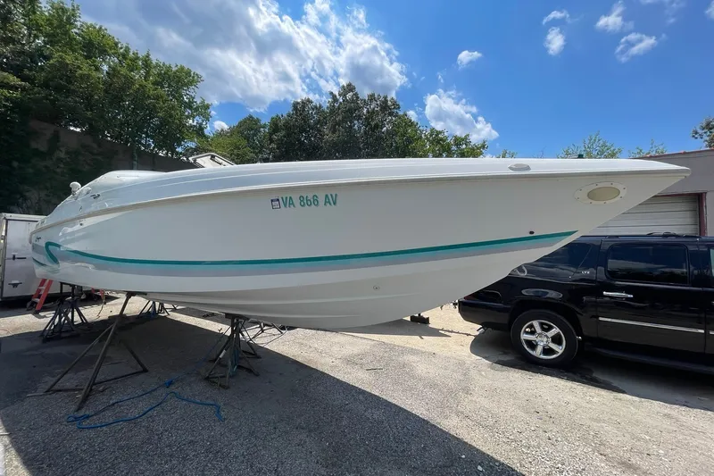 The Image of 1996 Baja 322 boat on stands, white hull with teal accents, parked outdoors. - 1