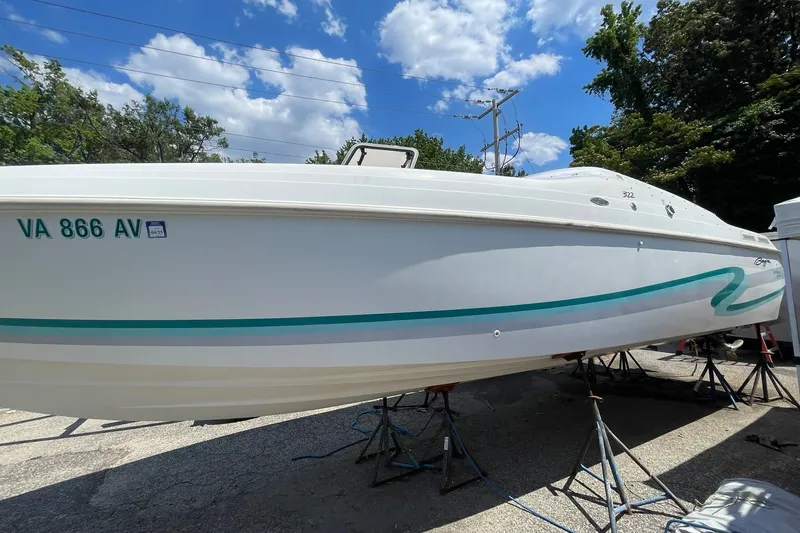Slide: The Image of 1996 Baja 322 boat on stands, white with teal accents, under a clear blue sky. - 19