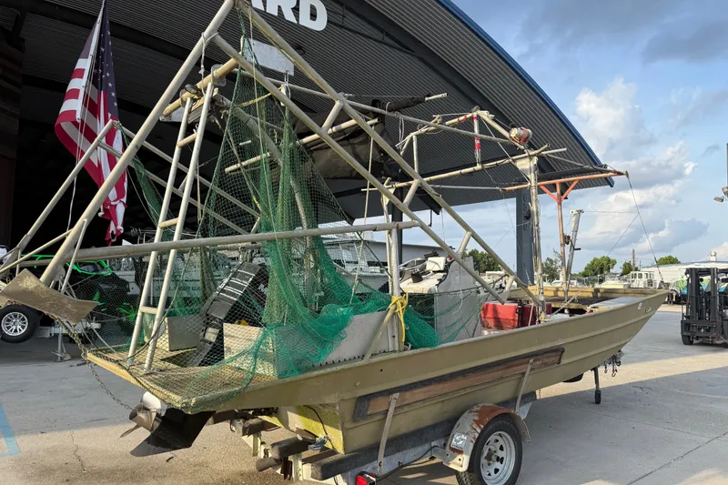 Slide: The Image of 1984 Alweld 1852PF boat with netting and equipment, parked on a trailer near a hangar. - 3