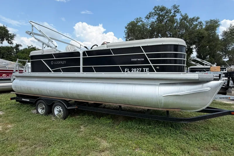 The Image of 2022 Sweetwater 2286 SBX pontoon boat on trailer, parked on grass under a blue sky. - 0