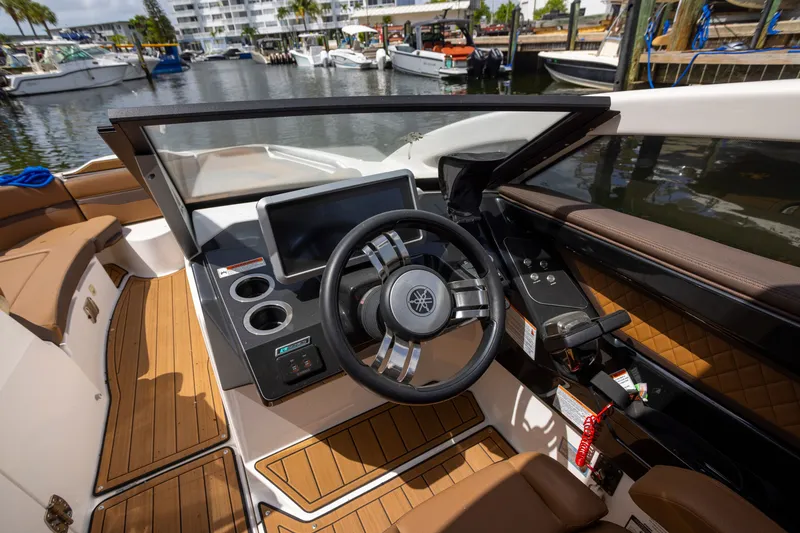 Slide: The Image of 2024 Yamaha Boats 275SE helm with modern steering wheel and dashboard, docked at marina. - 5
