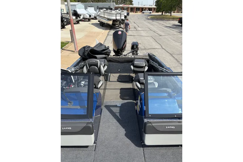 Slide: The Image of 2024 Lund 202 Pro-V GL boat with dual consoles and seating, parked outdoors. - 7