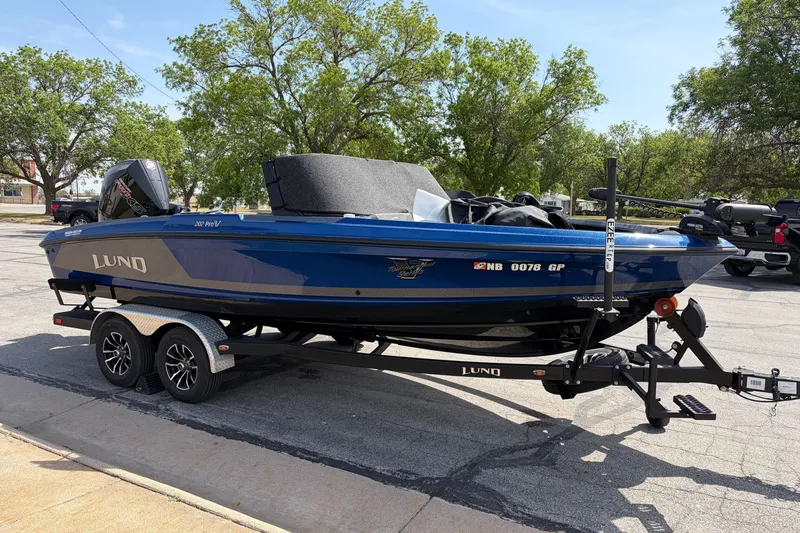 Slide: The Image of 2024 Lund 202 Pro-V GL boat on trailer, parked outdoors with trees in background. - 3