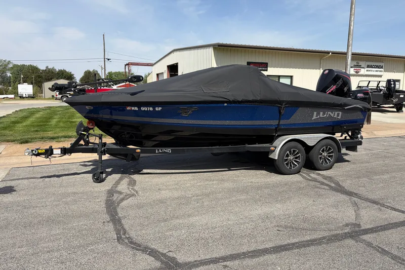 The Image of 2024 Lund 202 Pro-V GL boat on trailer, covered, parked outside dealership. - 1