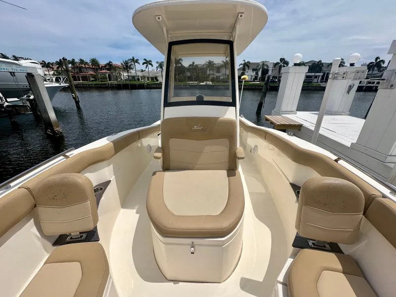 Slide: The Image of The image shows the cockpit of a 2019 Scout 235 XSF boat. It features beige upholstery and is docked at a marina. - 5