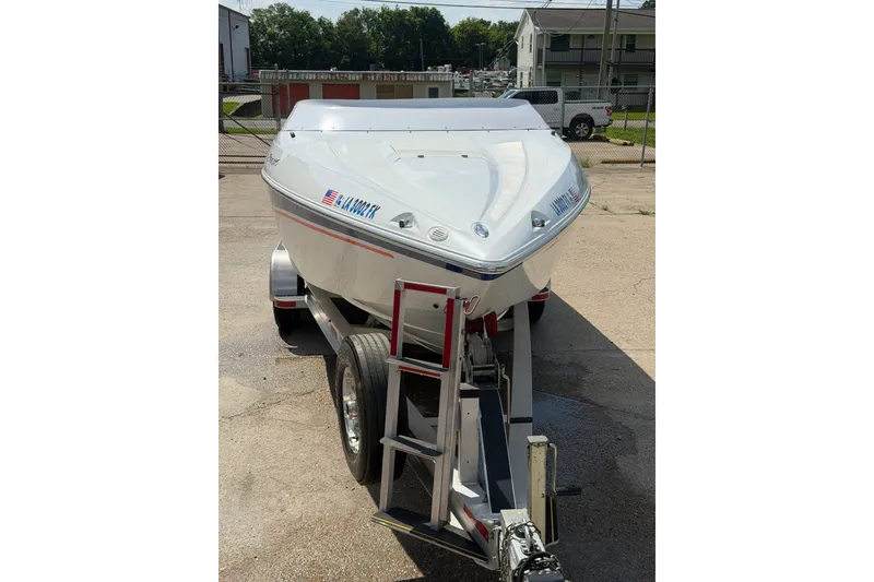 Slide: The Image of 2004 Baja 245 Performance boat on trailer, parked outdoors in a sunny setting. - 2
