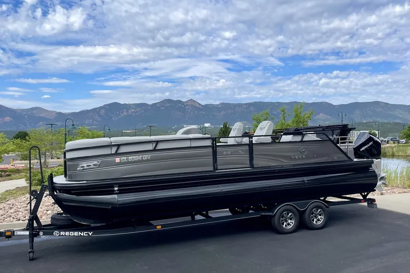 The Image of 2023 Regency 250LE pontoon boat on trailer with scenic mountain backdrop. - 1