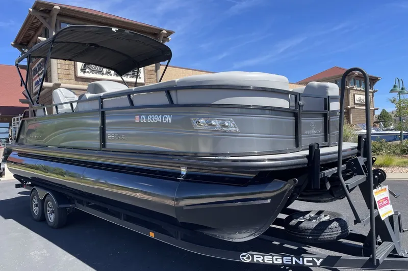 Slide: The Image of 2023 Regency 250LE pontoon boat on trailer, parked outdoors under clear sky. - 1