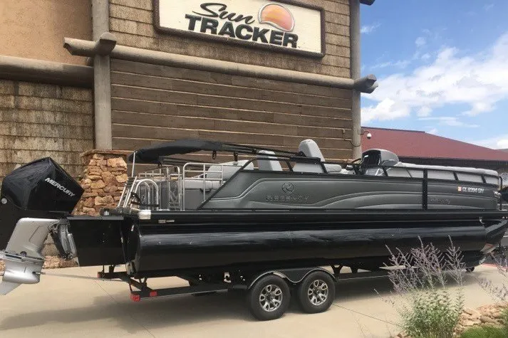 Slide: The Image of 2023 Regency 250LE pontoon boat on trailer outside Sun Tracker dealership. - 6