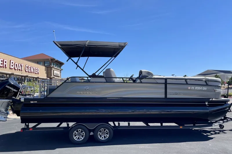 Slide: The Image of 2023 Regency 250LE pontoon boat on trailer at a boat center under clear blue sky. - 2