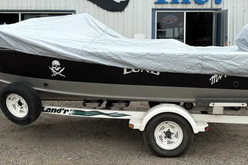 Slide: The Image of 2001 Lund Mr. Pike 16 boat on trailer, covered, outside a building with open sign. - 13