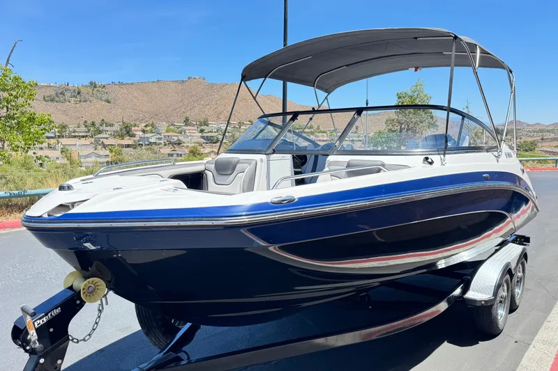 Slide: The Image of 2017 Yamaha Boats 212 Limited on trailer, sleek design, blue and white exterior, sunny day. - 3