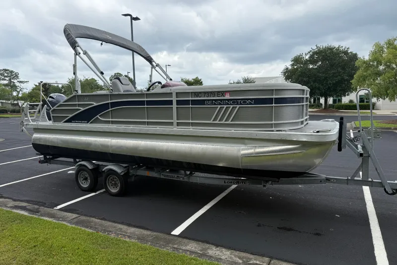 Slide: The Image of 2022 Bennington LX 22 Swingback pontoon boat on trailer in parking lot. - 10