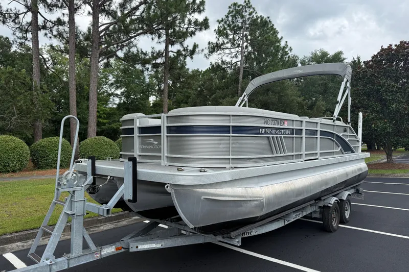 Slide: The Image of 2022 Bennington LX 22 Swingback pontoon boat on trailer in a parking lot. - 3