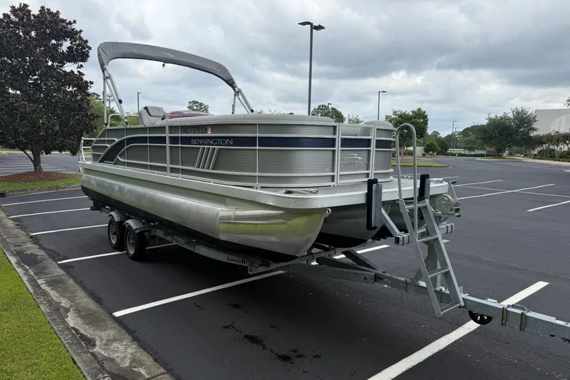 Slide: The Image of 2022 Bennington LX 22 Swingback pontoon boat on trailer in parking lot. - 11