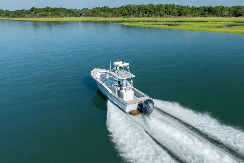 Slide: The Image of 2023 Harrison Boatworks 28 cruising on a serene lake with lush green shoreline. - 34