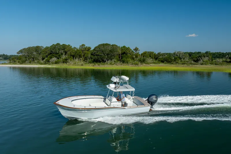 Slide: The Image of 2023 Harrison Boatworks 28 cruising on a serene lake with lush green shoreline. - 5