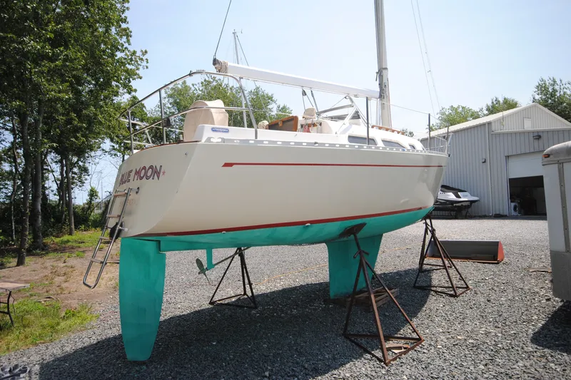 The Image of 1987 Tillotson-Pearson 28 sailboat on stands, outdoors near a storage building. - 0